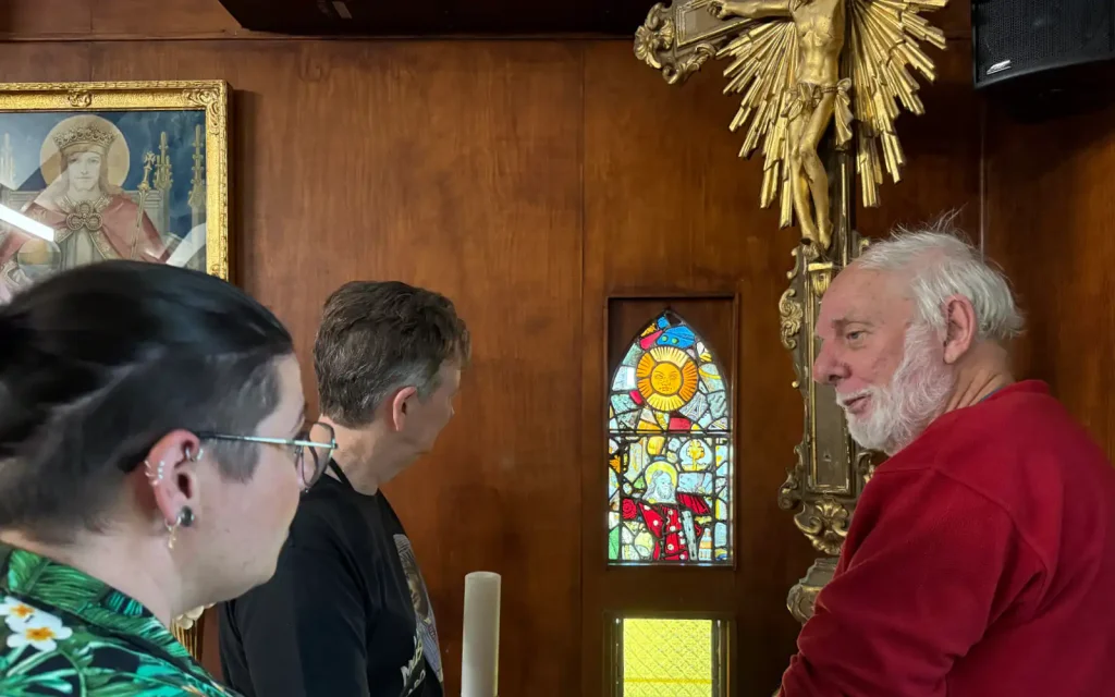 Guide speaking with visitors beside a small coloured stained glass window and candle