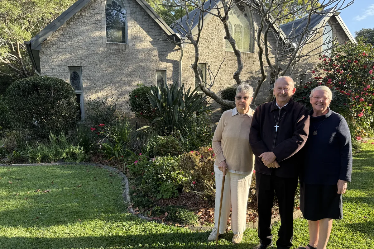 Three Abbey Community members standing outside The Abbey Church in the Caboolture gardens